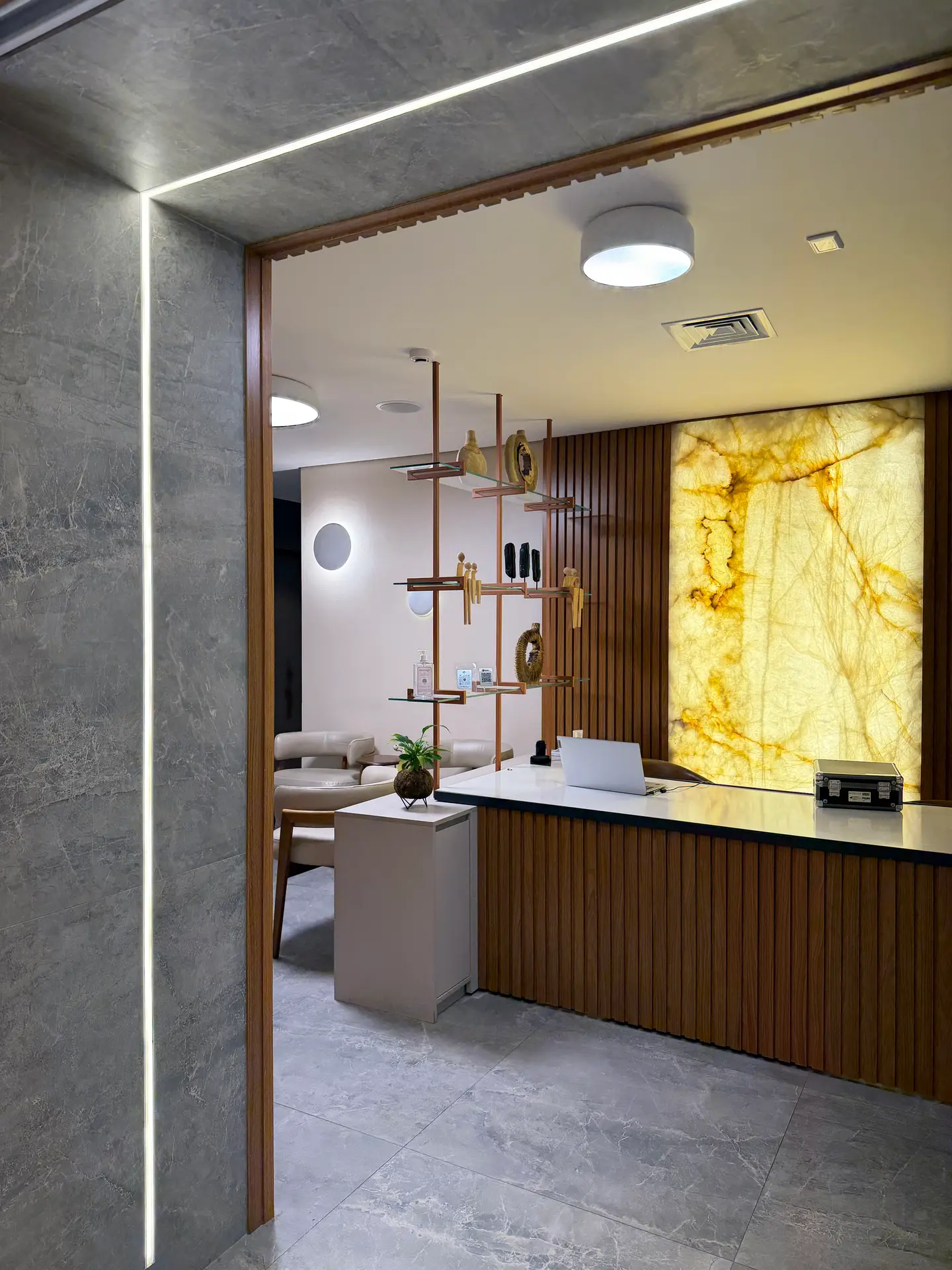 Recepção do consultório, com balcão de madeira e painel de pedra iluminado